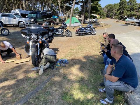 Riders taking a break on the grass beside parked motorcycles.