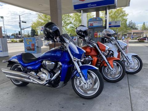 Blue and orange motorcycles parked beneath a fuel-station canopy.