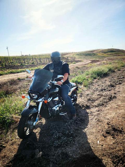 A rider seated on a motorcycle beside an open field.