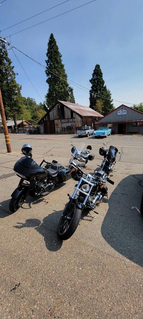 Motorcycles parked beside an outdoor stop beneath trees.