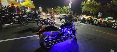 A purple-lit motorcycle at an outdoor gathering after dark.