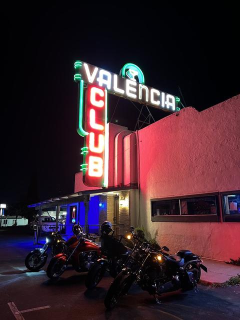 Motorcycles beneath an illuminated sign at night.