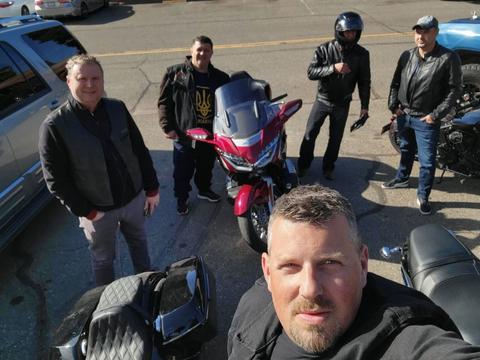 Riders gathered around motorcycles in a daytime group photo.