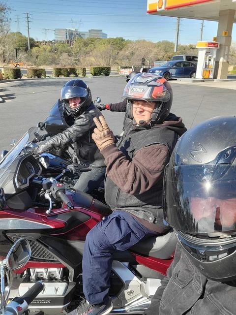 Helmeted riders seated on motorcycles at a fuel stop.