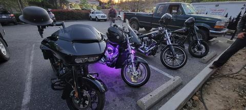Several motorcycles with purple accent lighting in a parking area.