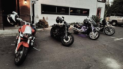 Riders and motorcycles beside a building in overcast light.