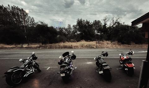 Four motorcycles parked beside a road under cloudy skies.