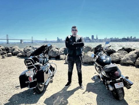 A person standing between motorcycles beside a waterfront.