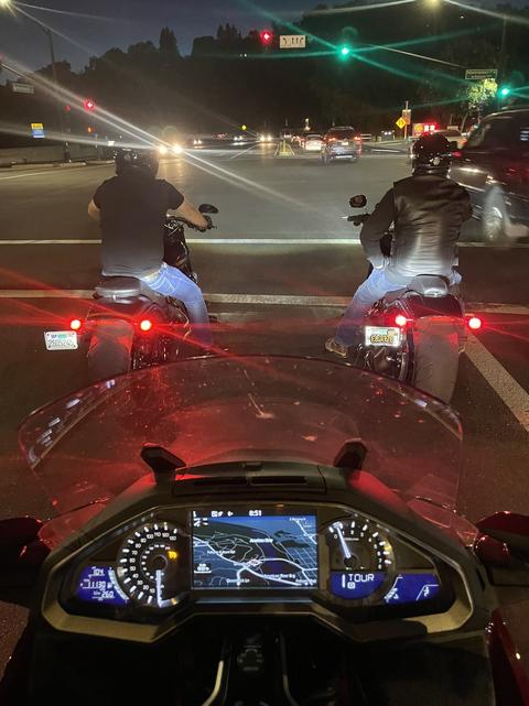 A view over a motorcycle dashboard toward nighttime traffic.