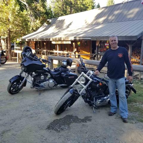 A person standing beside motorcycles outside a wooded stop.
