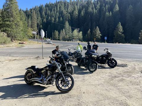 Motorcycles beside a mountain road with forested slopes behind.