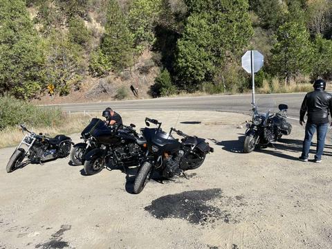 Another view of motorcycles beside a forested mountain road.