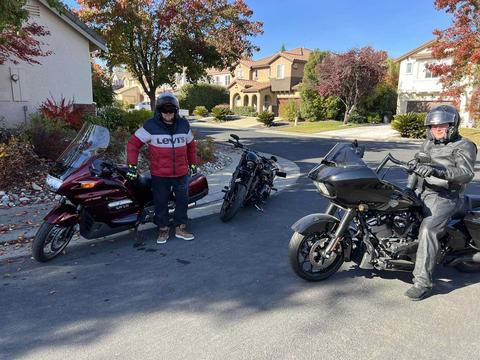 A rider standing beside motorcycles on a neighborhood street.