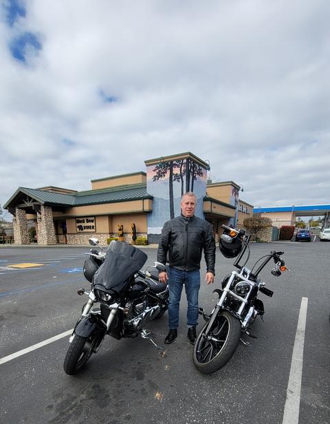 A person standing between motorcycles in a shopping-center lot.