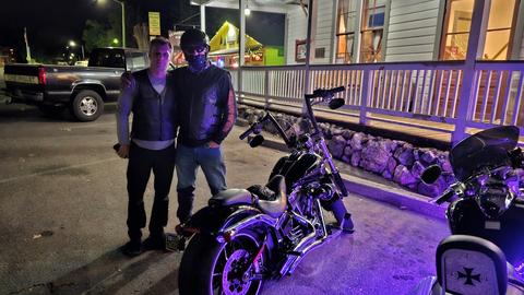 Two people standing beside a motorcycle in purple light.
