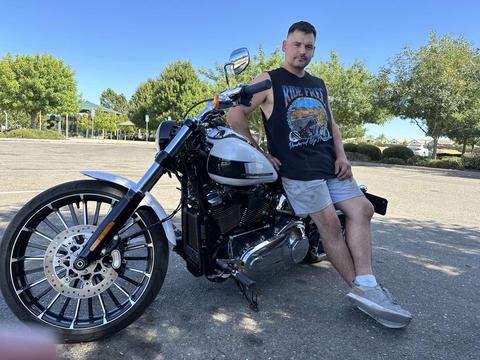 A person standing beside a black motorcycle on a sunny day.