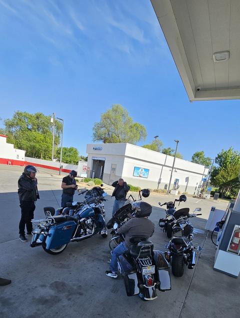 Riders with motorcycles beneath a fuel-station canopy.