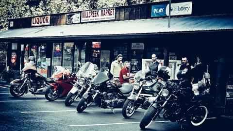 Riders and motorcycles outside a row of storefronts.