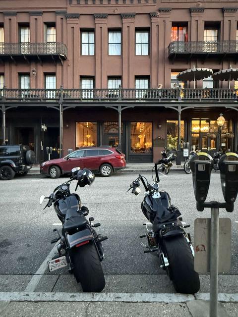 Two motorcycles parked across from a multistory brick building.